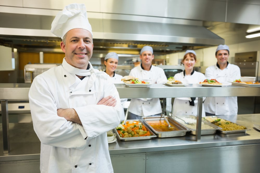 Proud mature head chef posing in a modern kitchen with his colleagues in the background