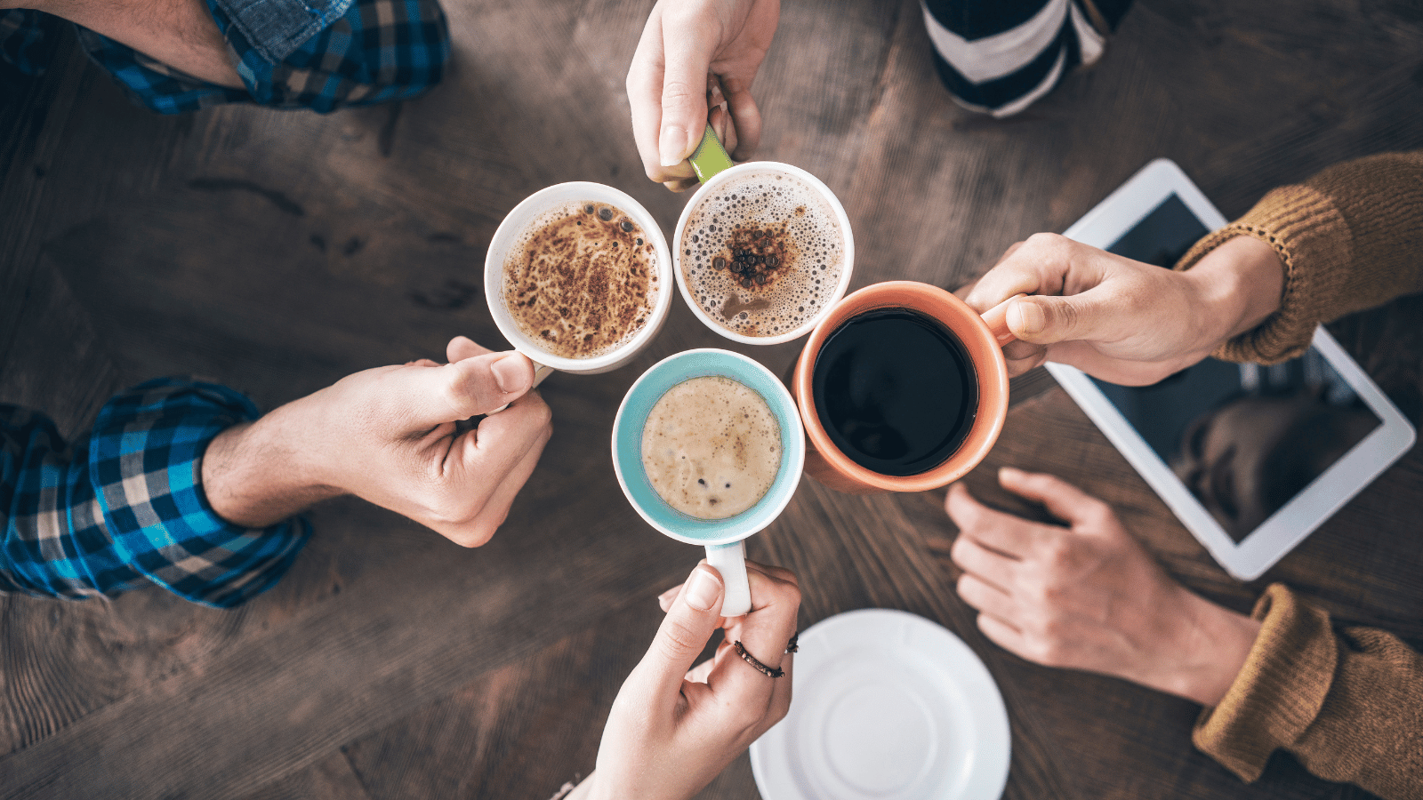 Four hands holding mugs of coffee and touching them together